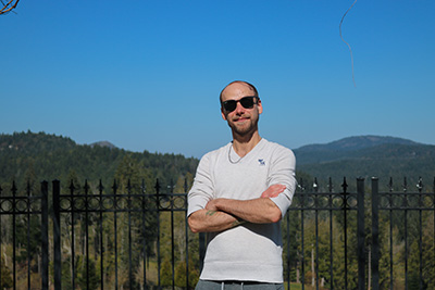 A picture of Scott Demeules with his arms crossed and sunglasses on with blue skies and grassy hills in the background.